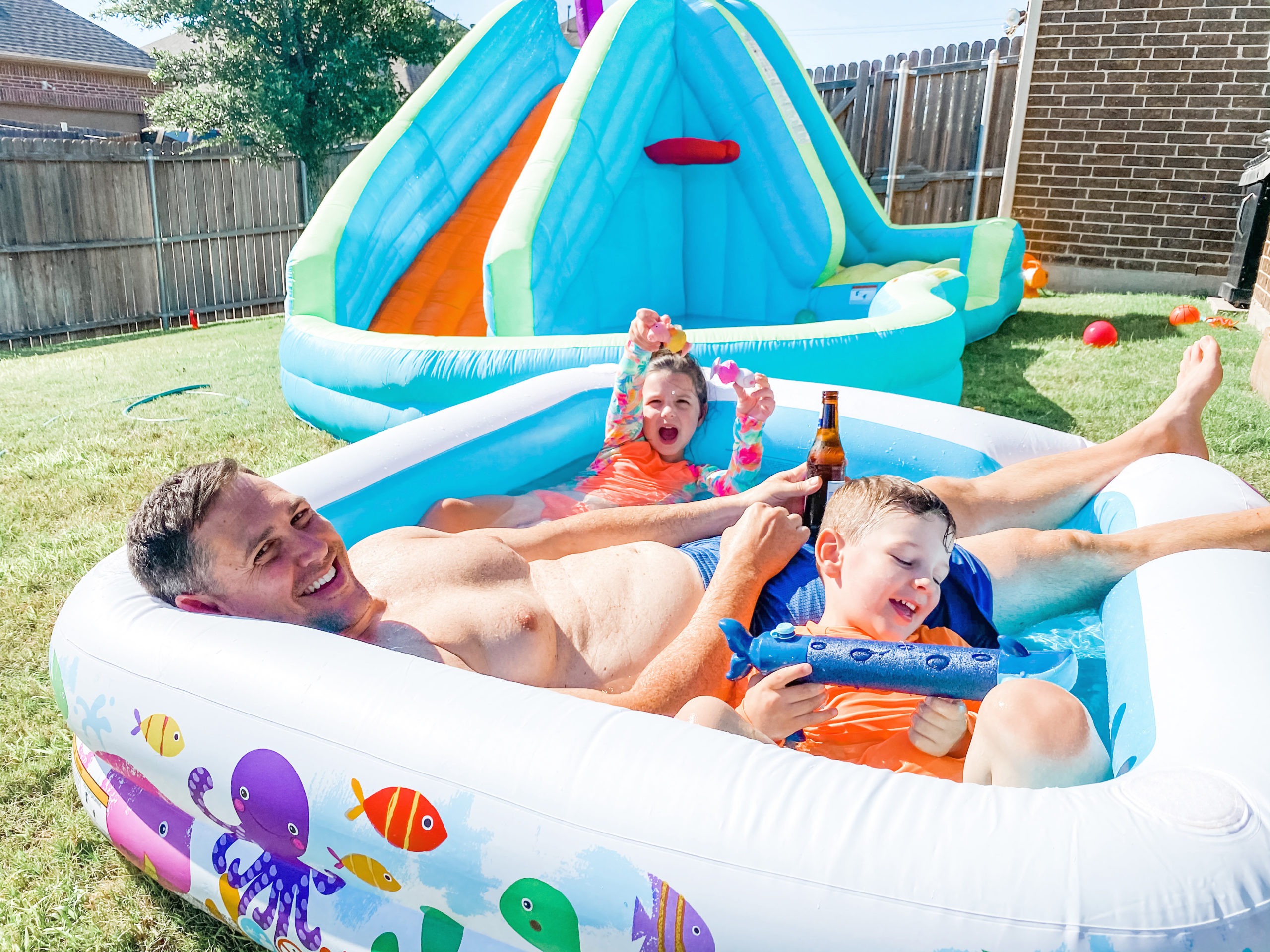 two kids and their dad in an inflatable pool in their backyard