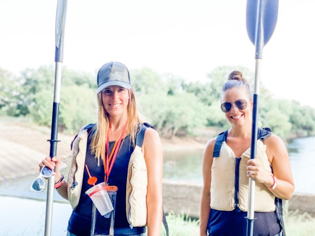 two girls wearing life vests holding kayak paddles