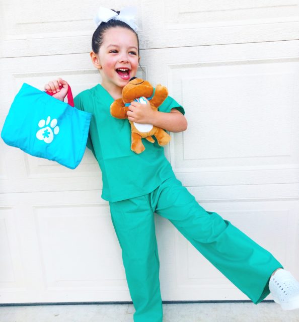 child dressed up as a vet holding a stuffed dog and vet kit